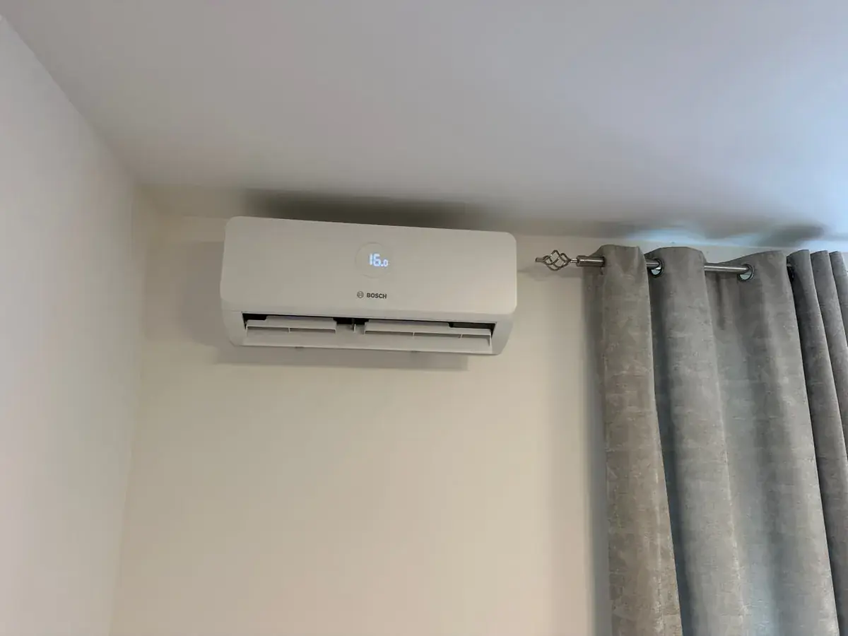 Bosch wall-mounted air conditioning unit beside grey curtains in a bedroom