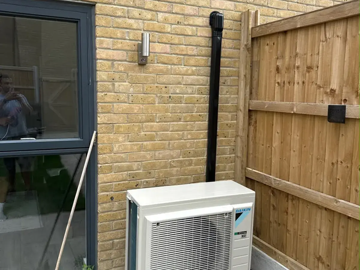 Daikin outdoor unit in a courtyard between a brick wall and a timber fence