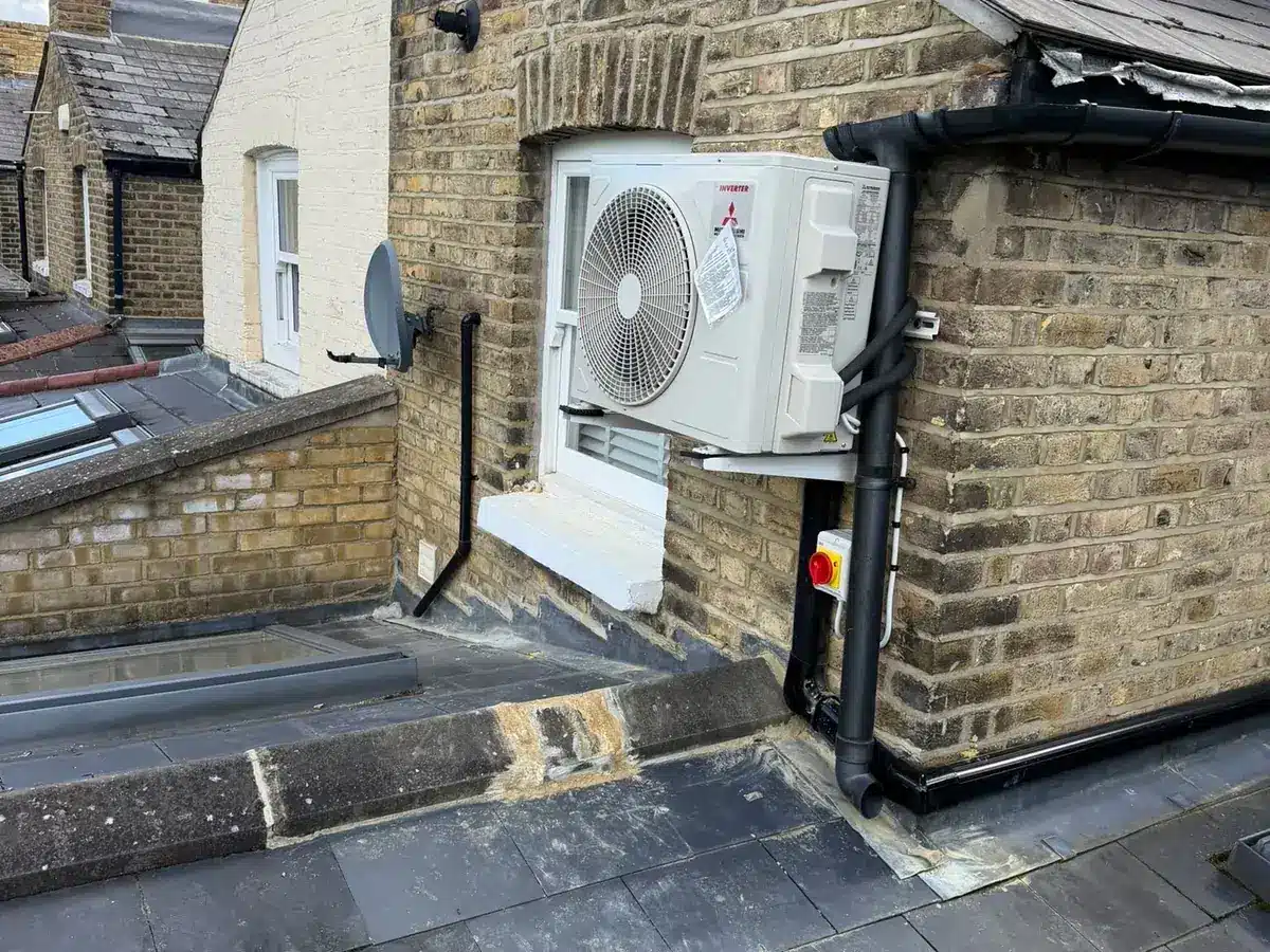 Mitsubishi Electric outdoor unit on wall brackets above a flat roof with black pipe trunking
