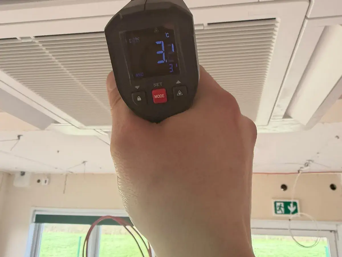 Infrared thermometer measuring the airflow temperature at a ceiling cassette unit