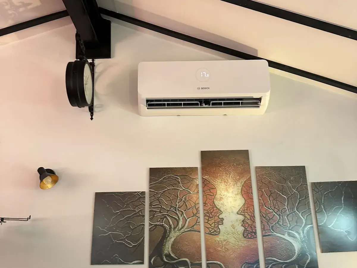 Wall-mounted air conditioning unit beside a wall clock above tree canvas artwork