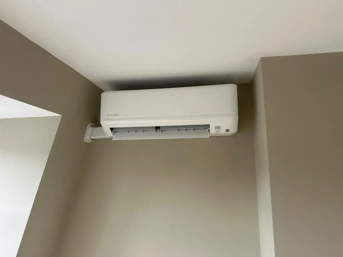 Wall-mounted air conditioning unit near the ceiling in a neutral-painted room