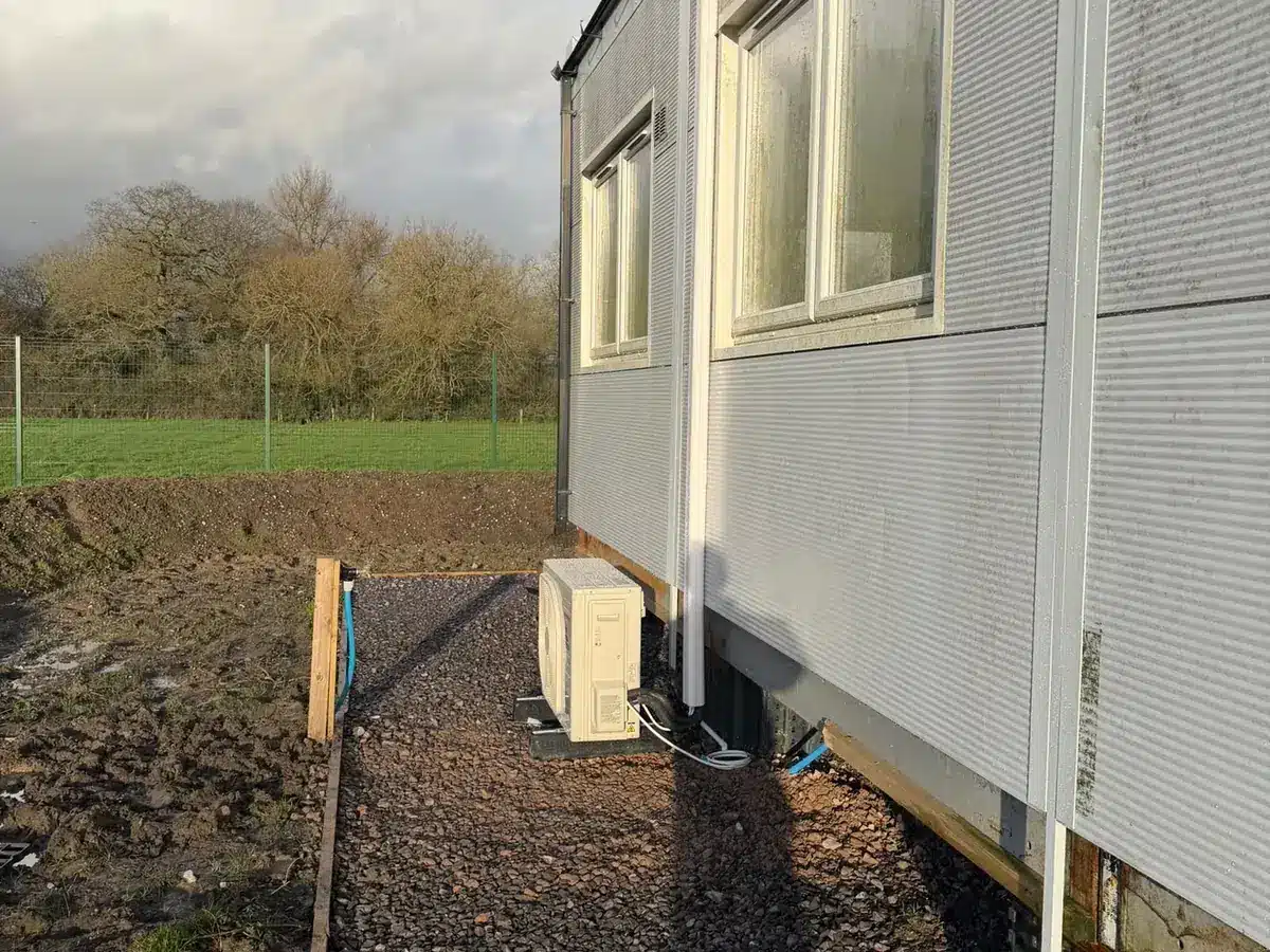 Outdoor unit on a gravel path beside a clad modular building next to a field