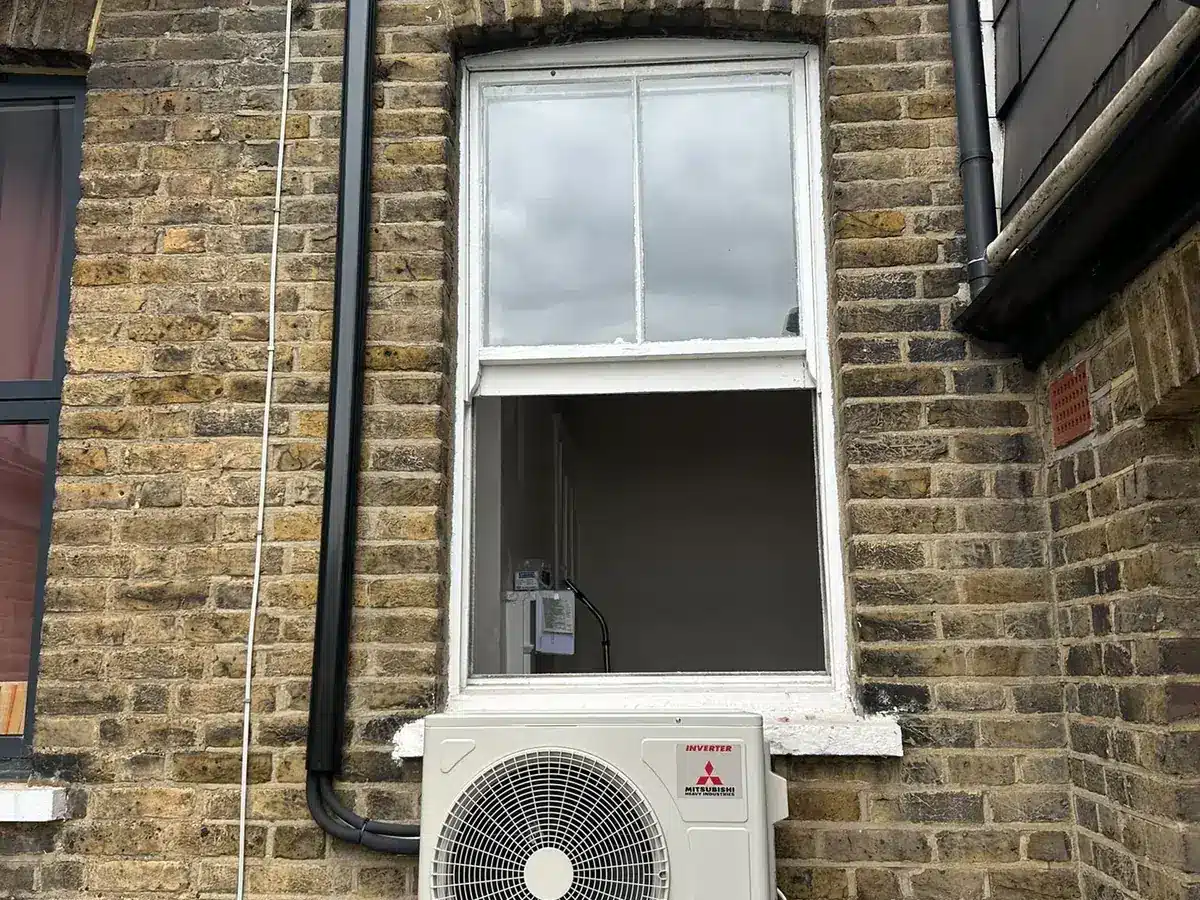 Mitsubishi Electric outdoor unit below a sash window on a yellow stock brick wall