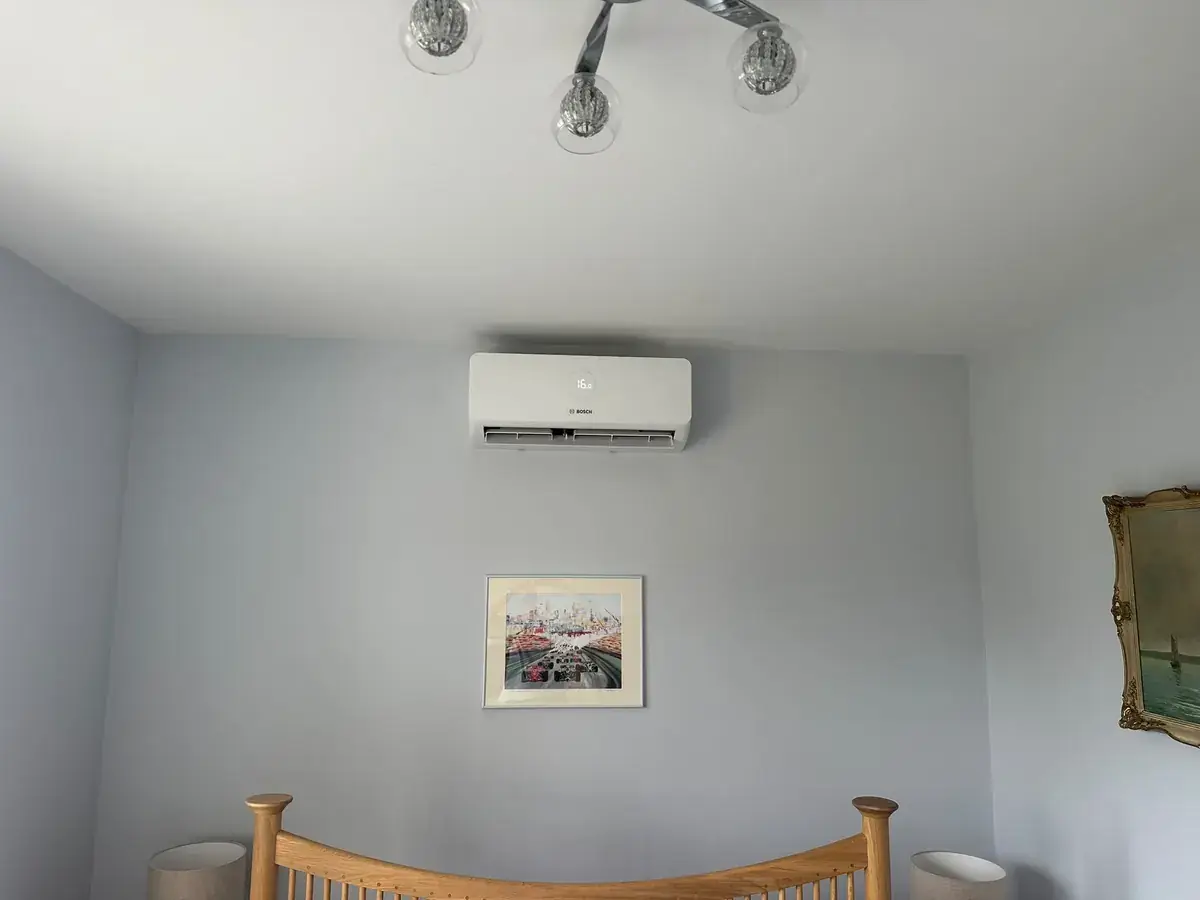 Wall-mounted air conditioning unit above a bed in a light blue bedroom
