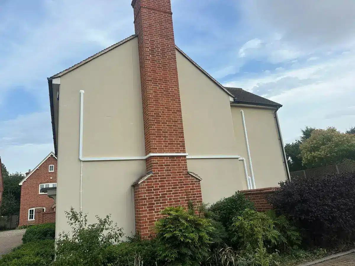 White pipe trunking across the gable wall of a rendered house with a brick chimney