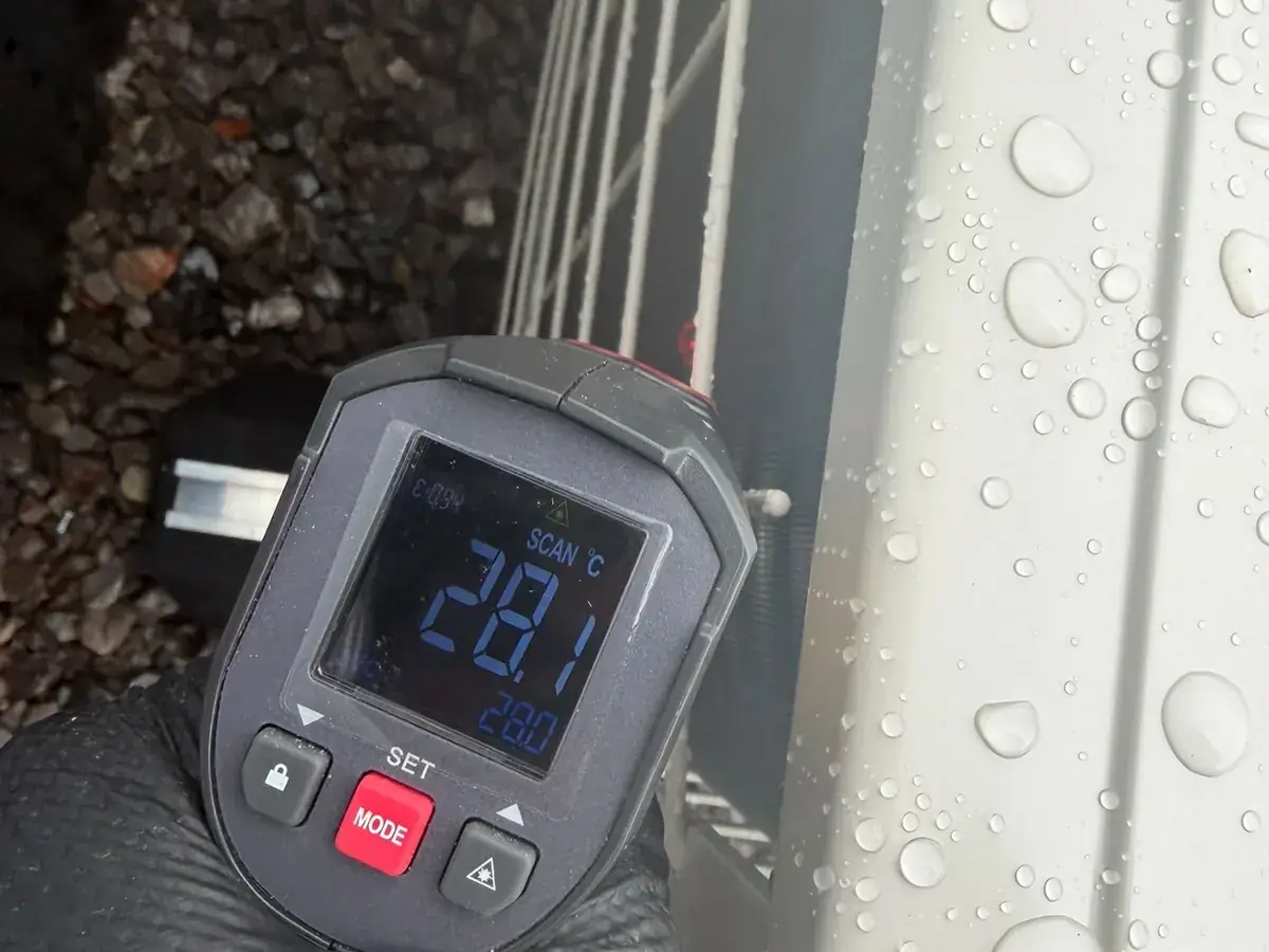 Infrared thermometer reading 28.1°C at an outdoor unit covered in water droplets