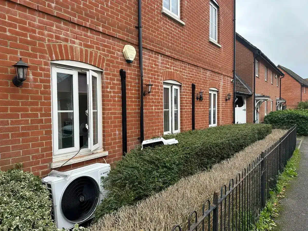 Outdoor unit beside a hedge in front of a row of red-brick houses