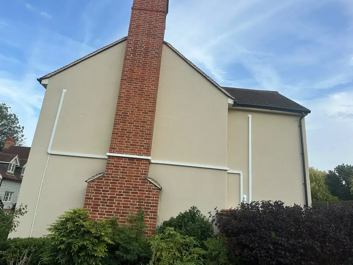 Gable wall of a rendered house with white pipe trunking beside a brick chimney