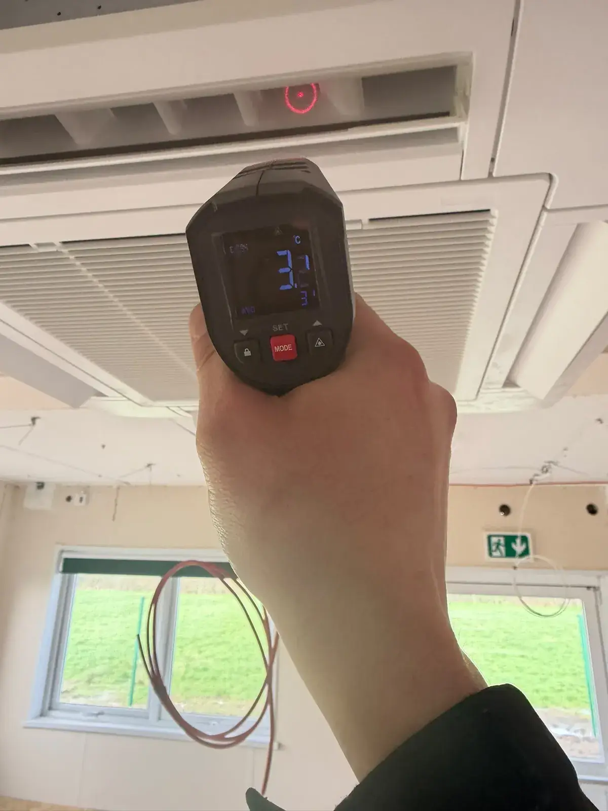 Engineer checking the air temperature at a ceiling cassette with an infrared thermometer
