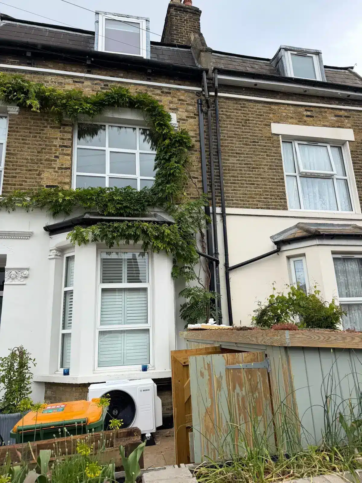 Outdoor air conditioning unit in the front garden of a Victorian terraced house with wisteria