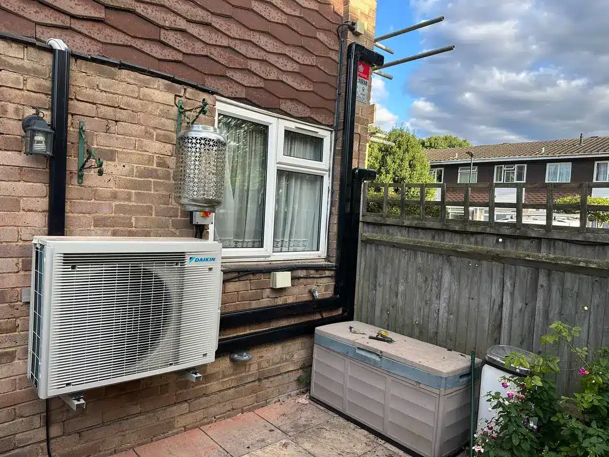 Daikin outdoor air conditioning unit mounted on a brick wall beside a patio door