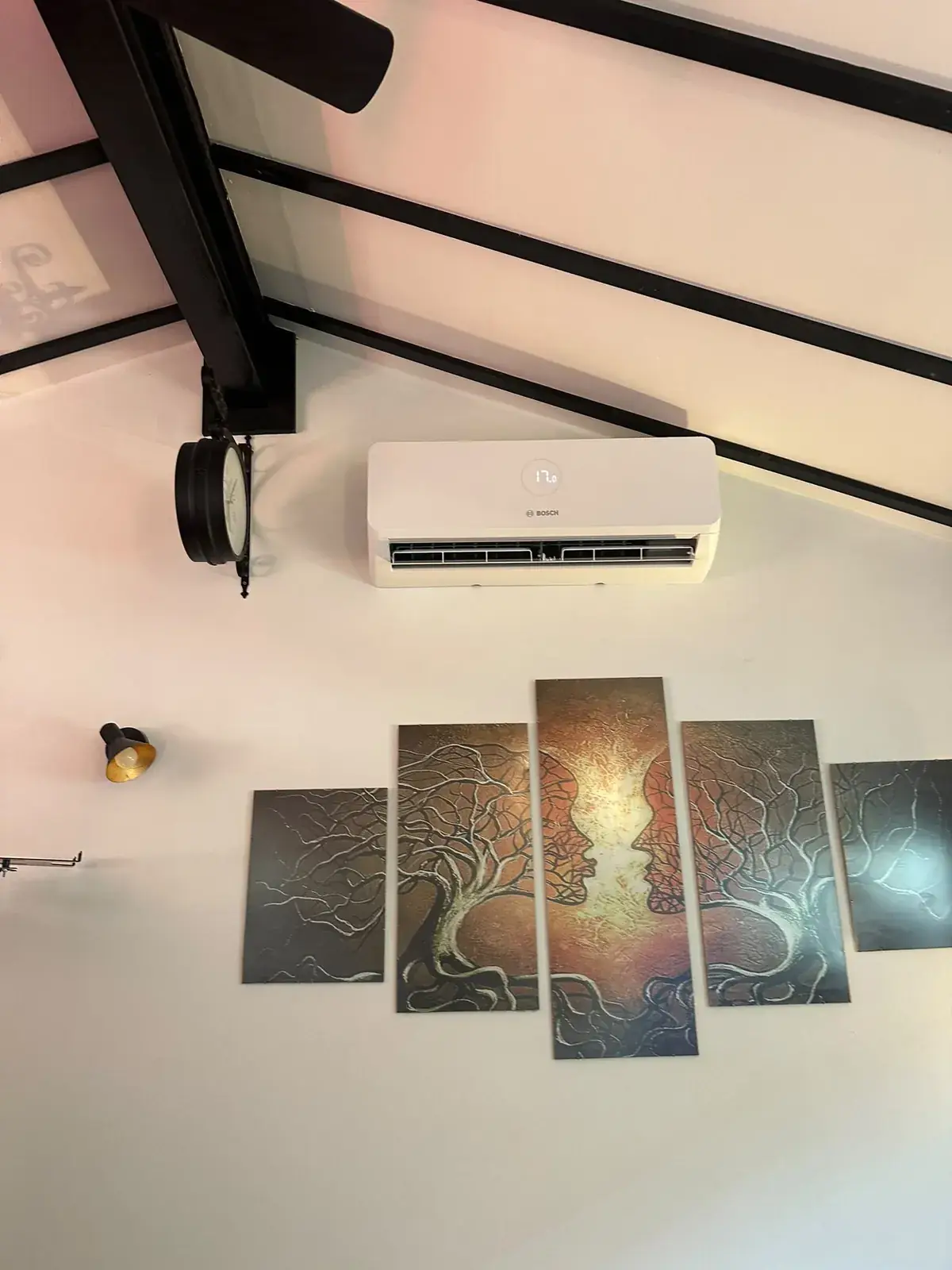 White wall-mounted air conditioning unit above multi-panel tree artwork in a room with exposed beams