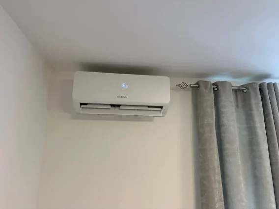 Bosch wall-mounted air conditioning unit beside grey curtains in a bedroom