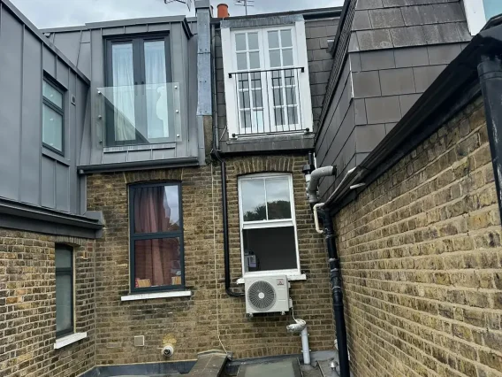 Outdoor unit mounted on the rear wall of a terraced house below a dormer extension