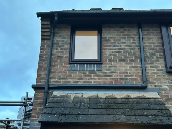 Dark pipe trunking routed across a brick house wall above a tiled bay roof