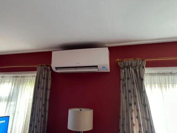 Wall-mounted air conditioning unit above curtained windows in a room with a red feature wall