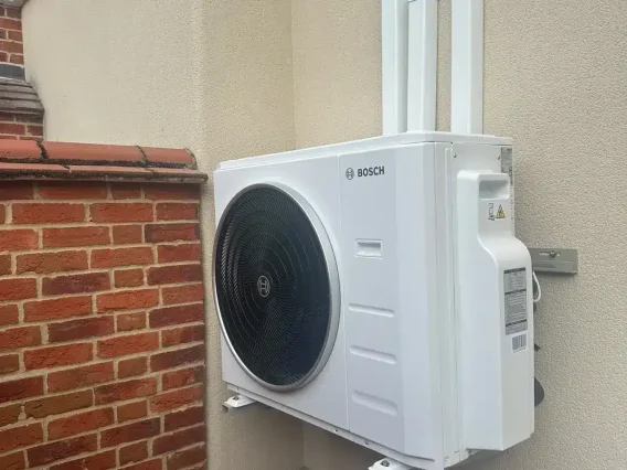 Bosch outdoor unit on wall brackets against a rendered wall with white pipe trunking