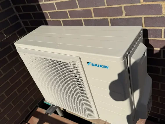 Daikin outdoor unit in sunlight against a dark brick wall